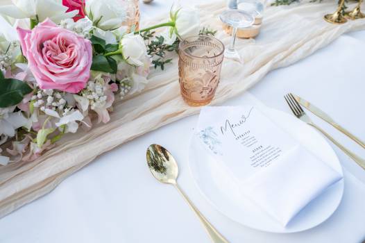 Elegant table setting featuring flowers, menu card, and gold utensils on a white tablecloth.