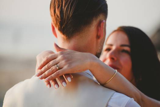 A couple looks at each other tenderly, sharing a moment of love with a beautiful beach background. The wedding rings are visible.