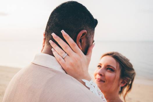 A bride gazes lovingly at her groom, their intimate moment captured against a serene beach backdrop.