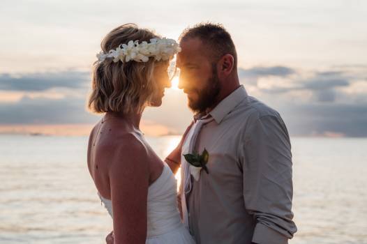 A couple shares a romantic moment by the water at sunset, gazing into each other's eyes, surrounded by nature's beauty.