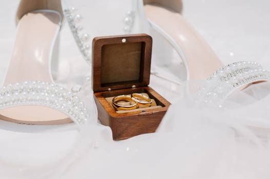 Elegant wedding rings in a wooden box, nestled between beautiful bridal shoes adorned with pearls.