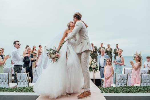 A joyful wedding moment with a couple embracing, surrounded by guests applauding in a beautiful outdoor setting.