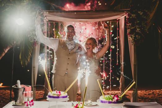 A joyful couple celebrates with sparklers and fireworks at their wedding, surrounded by festive decorations.