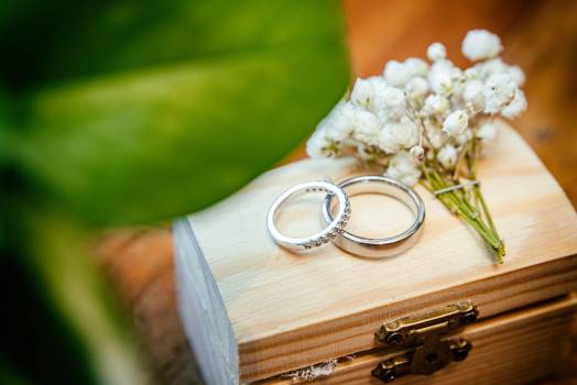 Two elegant rings resting on a wooden box, surrounded by delicate white flowers and greenery.