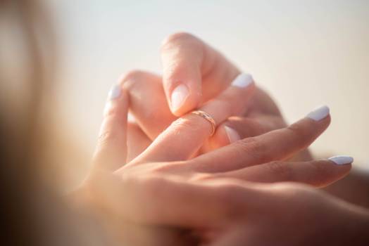 A close-up of two hands, one placing a ring onto a finger, symbolizing love and commitment. Soft background focus.