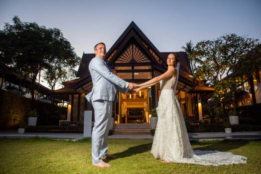 A happy couple holds hands, celebrating together in front of a beautiful house at twilight.