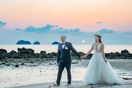 A couple walks hand in hand on the beach at sunset at koh samui, surrounded by serene waters and distant islands.