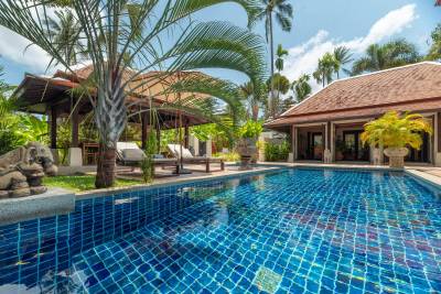 A tranquil villa with a sparkling turquoise pool, surrounded by lush greenery and palm trees under a sunny sky.