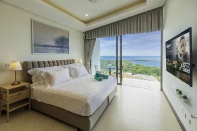 A modern bedroom with a sea view, featuring a large bed, TV, and balcony with outdoor seating.