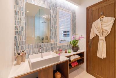 Stylish bathroom featuring a modern sink, decorative tiles, plants, and wooden accents. Relaxing and inviting space.