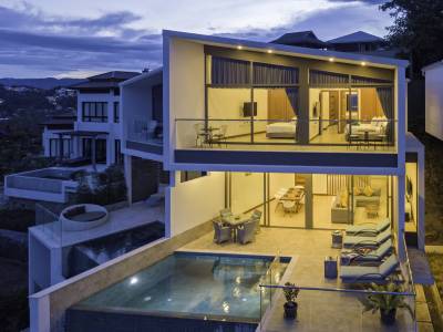 A modern villa with a pool, panoramic views, and large glass windows at dusk, showcasing sleek architecture.