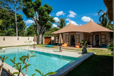 A tranquil outdoor space featuring a pool, a tent-like structure, and lush greenery under a bright blue sky.