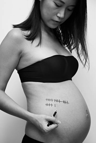 A pregnant woman marks her belly with tally lines, capturing moments of her pregnancy in a black-and-white photo.