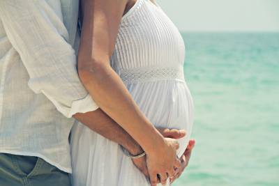 A couple embraces at the beach, gently touching a pregnant belly, celebrating love and new beginnings.